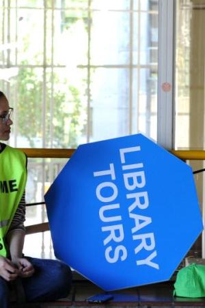 two library buddies seated. One holds a library tour signboard